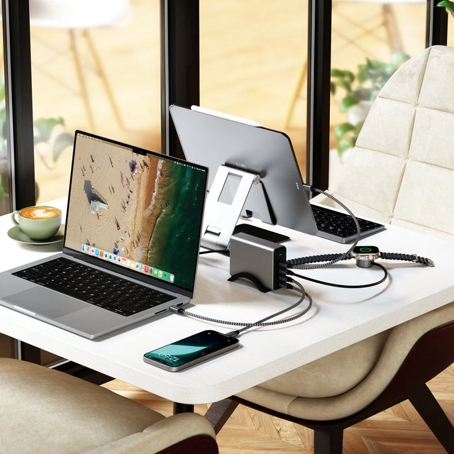 Satechi 165W USB‑C 4‑Port PD GaN Charger powering a MacBook, iPad, and iPhone on a café‑style desk setup, showing multiple devices charging simultaneously