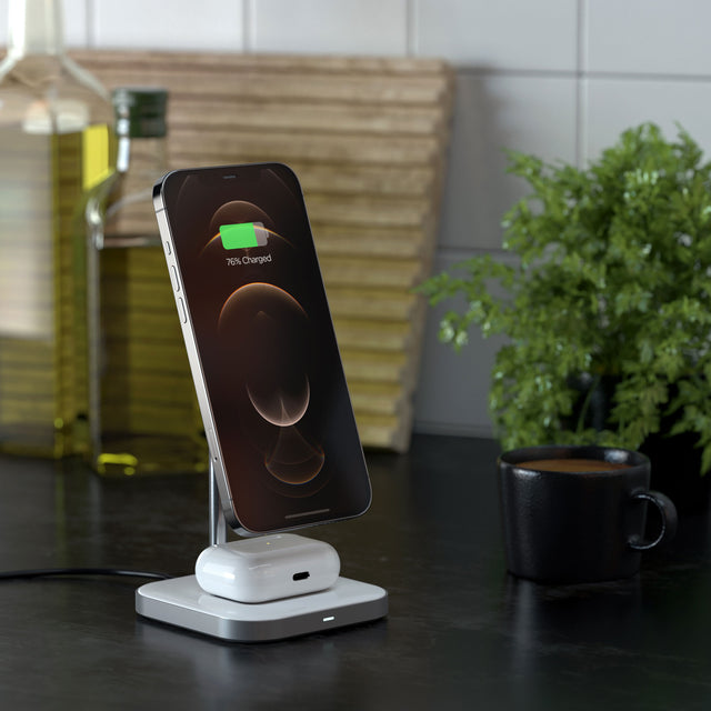 Satechi Aluminum 2-in-1 Magnetic Wireless Charging Stand charging an iPhone and AirPod, the iPhone is displaying charging status on a kitchen counter.