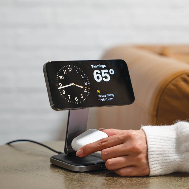 iPhone with a Satechi 2-in-1 Foldable Qi2 Wireless Charging Stand showing 
 weather information on a table, with a person's hand interacting with it.