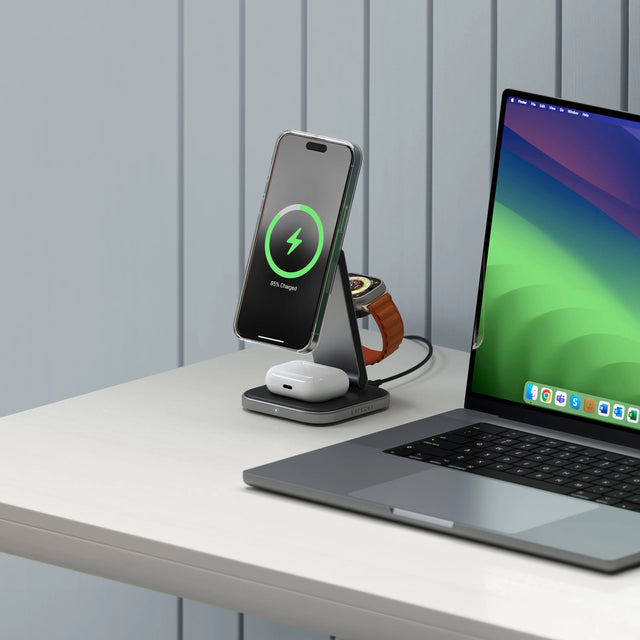 MacBook on a desk with a 3-in-1 Foldable Qi2 Wireless Charging Stand charging an iPhone, Apple Watch, and AirPods.