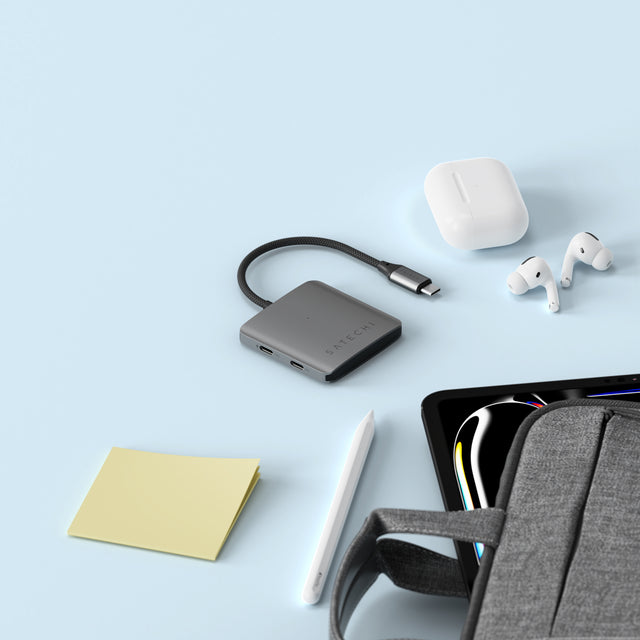Satechi 4‑Port USB‑C Hub with Power Delivery placed on a light blue surface alongside earbuds, a tablet stylus, sticky notes, and a tech bag, highlighting its compact and travel‑friendly design.