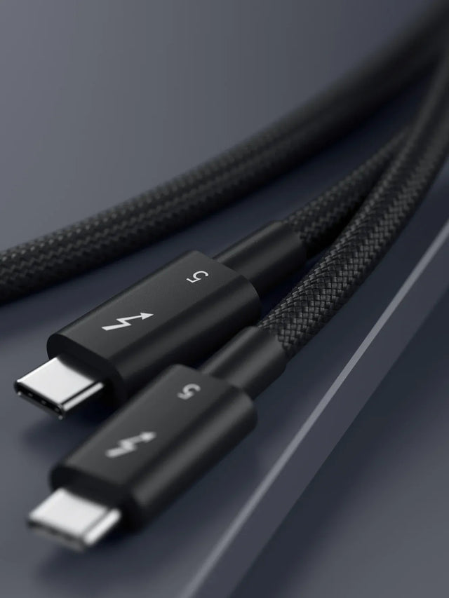 Close-up of a black Thunderbolt 5 Pro Cable on a dark surface showcasing the premium braided cable with reinforced strain relief and aluminum housing.