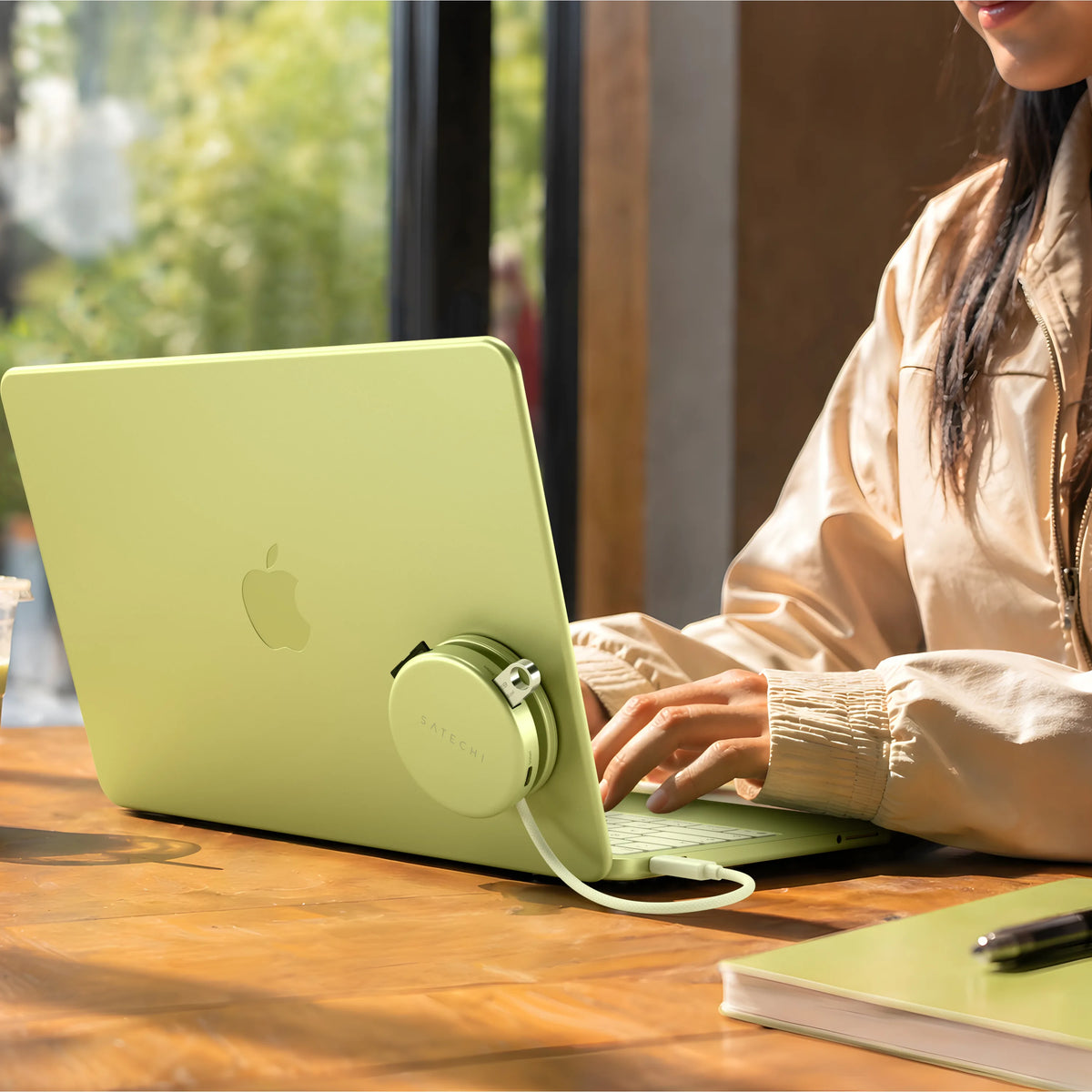 A person typing on an Citrus MacBook Neo at a wooden table with a matching Citrus OntheGo™ 5-in-1 Multiport Adapter  mounted on the lid and a braided cable attached. 