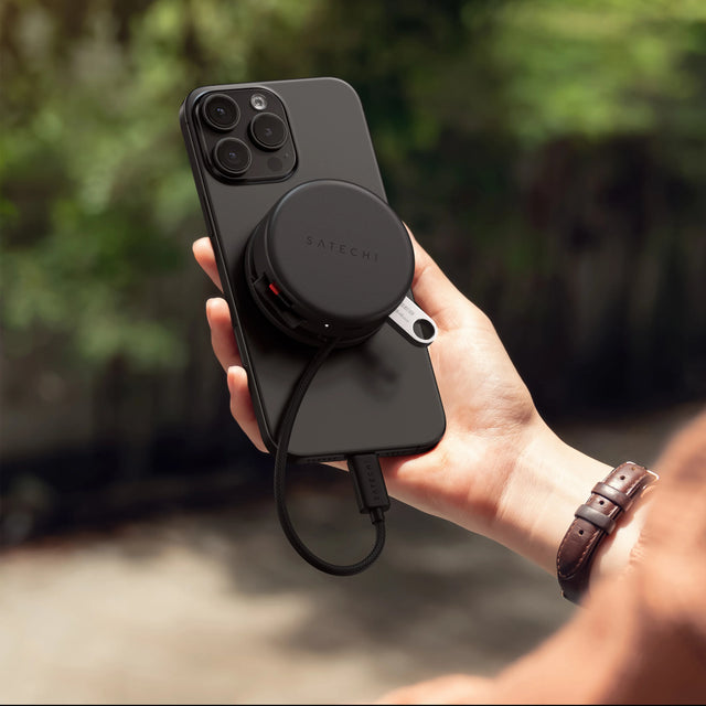 Satechi On-the-Go 7‑in‑1 Multiport Adapter magnetically attached to the back of a iPhone, with USB‑C cables plugged in for portable connectivity.