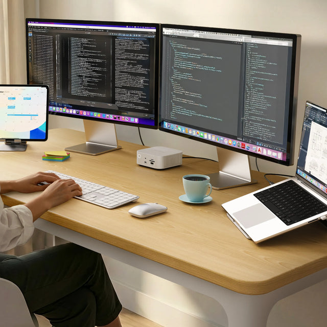 Close-up of a modern desk setup featuring the Thunderbolt 5 CubeDock™ with SSD Enclosure positioned beneath a widescreen monitor. The CubeDock’s front ports, including USB‑C, USB‑A, and SD card slots, are clearly visible. A slim external SSD enclosure sits to the right near a closed laptop stand, while small desk accessories like a plant, books, and a pen holder decorate the wooden surface.