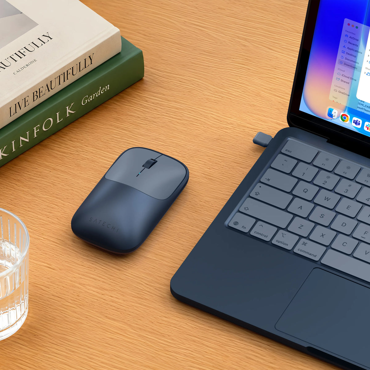 An Indigo Slim EX wireless mouse for MacBook Neo, with a 2.4GHz USB-C Receiver, beside an Indigo MacBook Neo on a wood desk.