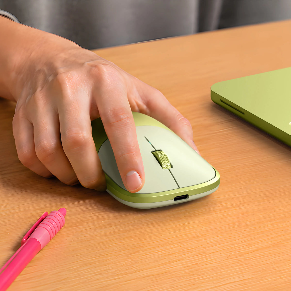 A hand using a Citrus Slim EX Wireless Mouse on a wooden desk.  The matching Citrus MacBook Neo is alongside alongside a pink pen in the foreground. 