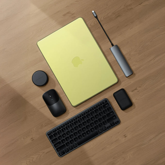 Top-down view of a Satechi workspace featuring a MacBook Neo on a light wood floor with a Satechi Slim EX1 Wireless Keyboard in dark, Slim EX Wireless Mouse, 7-in-1 USB-C Slim Multiport Adapter with Ethernet, and OntheGo™ 7-in-1 Multiport Adapter — best MacBook Neo accessories 2026.