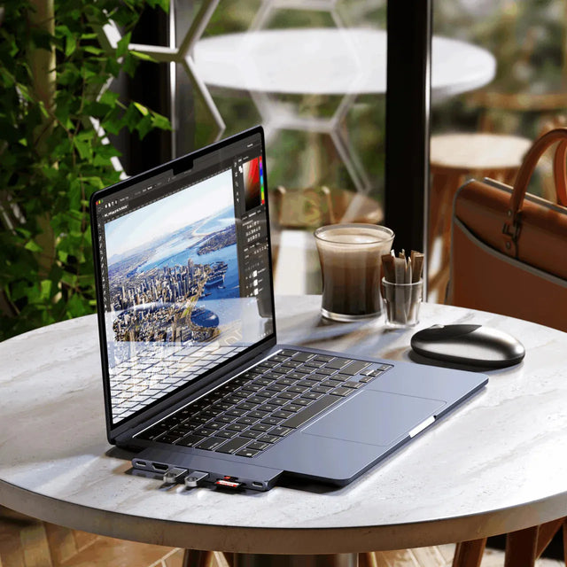 MacBook Air M2 in the Satechi Eco Hardshell Case on a café table, running a photo‑editing program and connected to several USB‑C devices and SD cards.