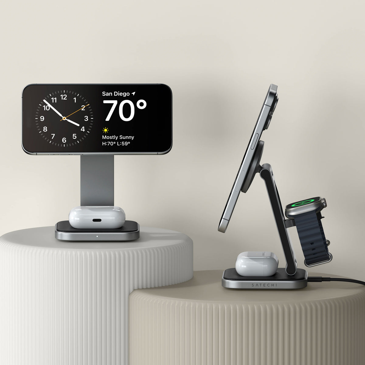 A 3-in-1 Qi2 wireless charging stand on a ribbed pedestal charging an iPhone that shows a weather widget reading "San Diego 70° Mostly Sunny H:70° L:59°," with AirPods charging at the base and an Apple Watch on the side mount.