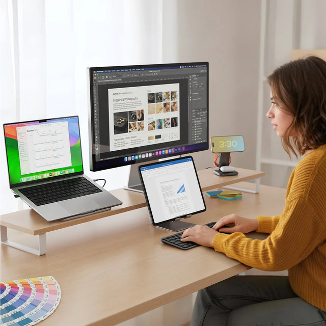 Person typing on Slim EX1 Wireless Keyboard, connected wirelessly to an iPad, MacBook, iPhone, and external monitor.