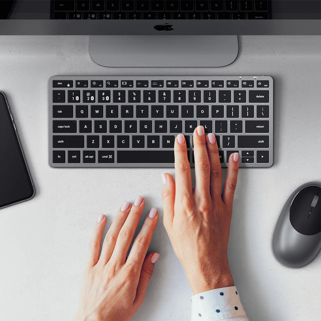 Person typing on a Slim X1 Bluetooth Backlit Keyboard next to M1 mouse on a desk.