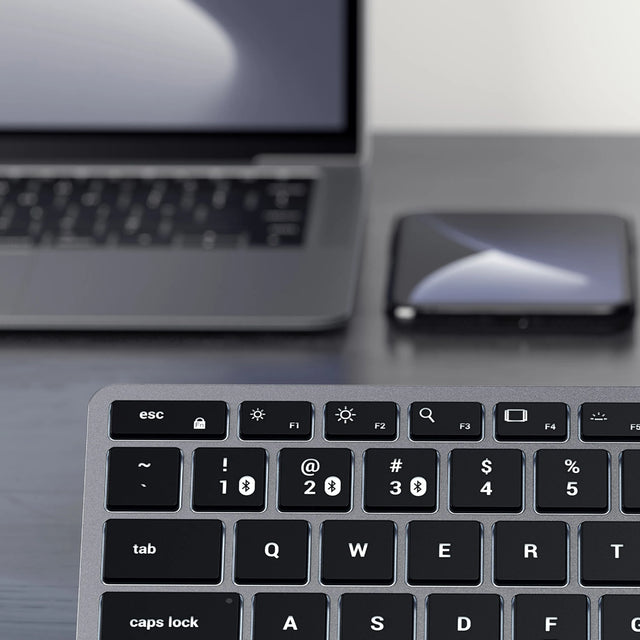 Close-up of Slim X1 Bluetooth Backlit Keyboard with a blurred smartphone and screen in the background.