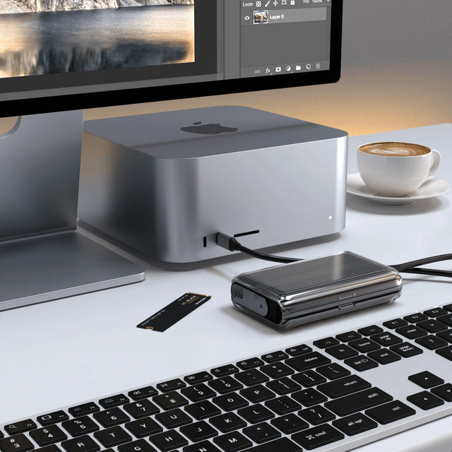 Satechi USB4 NVMe SSD Pro Enclosure connected to a Mac Studio, demonstrating extending storage for your professional work setup, shown next to an NVMe drive and a coffee cup.