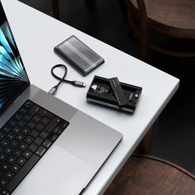 Open Satechi USB4 NVMe SSD Pro Enclosure on a desk beside a laptop, USB‑C cable, and NVMe drive ready for installation.