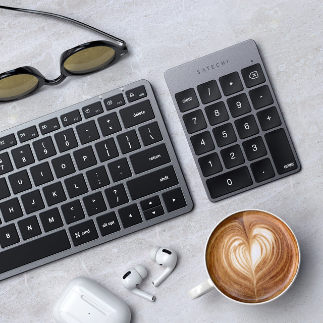 A Satechi Aluminum Slim Rechargeable Bluetooth Keypad alongside a Satechi slim keyboard, with sunglasses, coffee cup, and AirPods. 