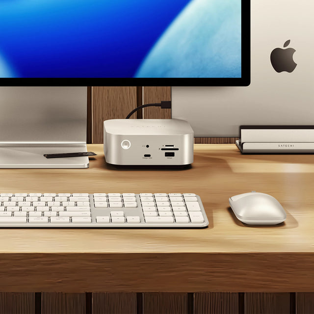 Close-up of a modern desk setup featuring the Thunderbolt 5 CubeDock™ with SSD Enclosure positioned beneath a widescreen monitor. The CubeDock’s front ports, including USB‑C, USB‑A, and SD card slots, are clearly visible. A slim external SSD enclosure sits to the right near a closed laptop stand.