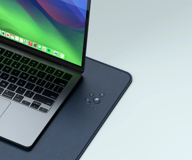 Close‑up of the Vegan‑Leather Premium Desk Mat with water droplets near a laptop, highlighting its smooth, durable, water‑resistant vegan‑leather material.