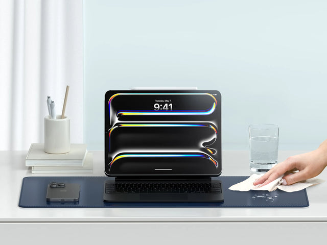 Vegan‑Leather Premium Desk Mat on a clean white desk with a tablet setup, as a hand wipes water droplets from its water‑resistant surface.