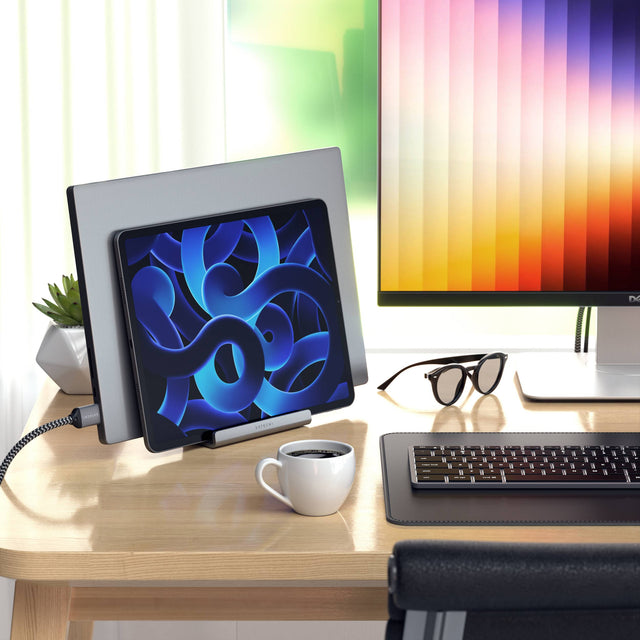 Satechi Dual Vertical Laptop Stand supporting a MacBook and iPad in a vertical position on a modern desk, shown next to a monitor, keyboard, and accessories.