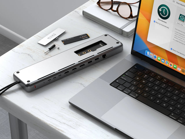 Open Satechi Dual Dock Stand on a desk with NVMe SSD and tools beside it, demonstrating the removable NVMe and M.2 SATA storage enclosure.