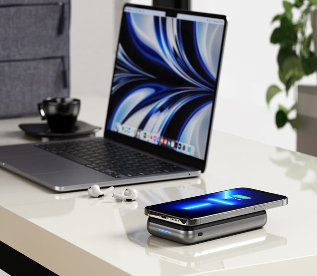 Satechi Duo Wireless Charger Power Stand placed on a desk wirelessly charging an iPhone beside a laptop and earbuds.