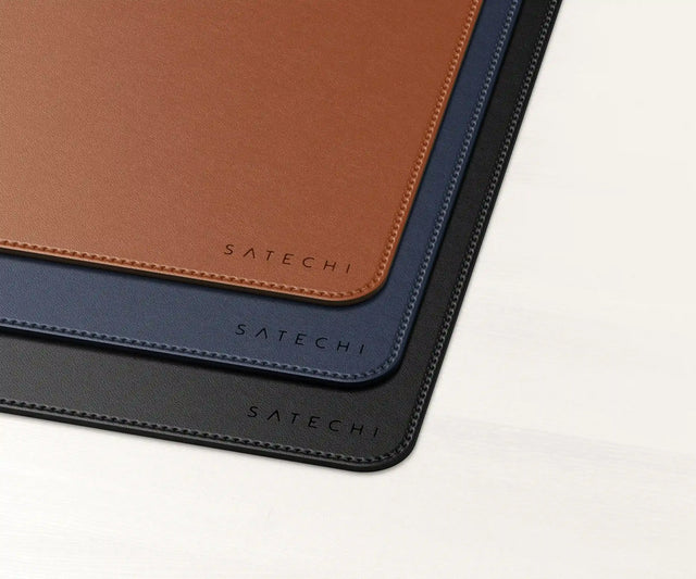 Vegan‑Leather Premium Mouse Pad displayed in black, navy, and brown finishes, showing stitched edges and the Satechi logo in the bottom corner.