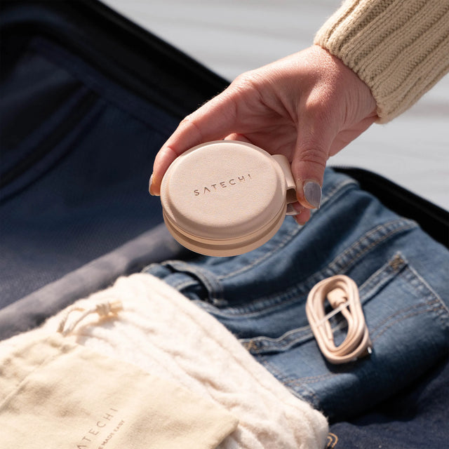 Hand holding a folded OntheGo™ 2-in-1 Charger over a suitcase full of clothes.