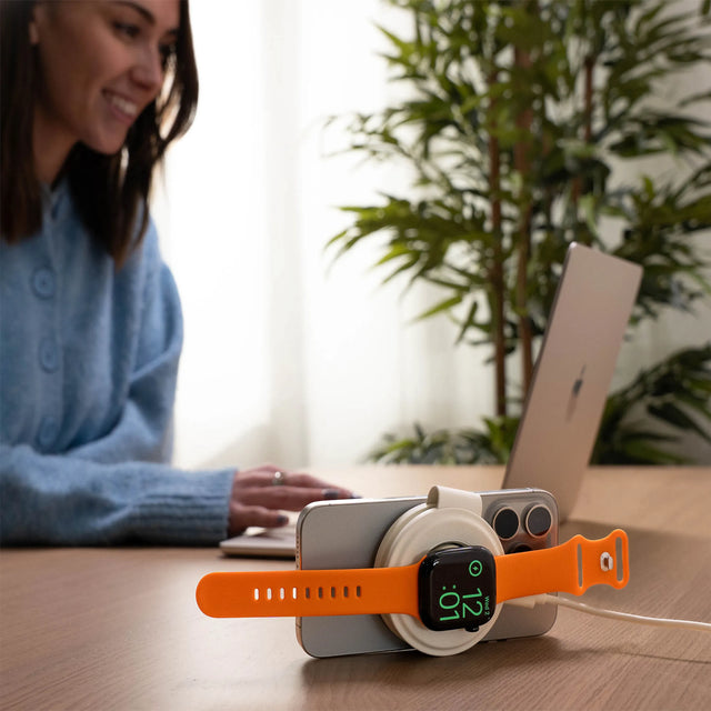Woman using a laptop and charging her iPhone and Apple Watch on a Satechi OntheGo™ 2-in-1 Charger simultaneously. 