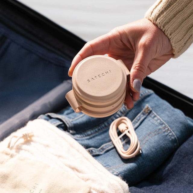 Hand holding a folded OntheGo™ 3-in-1 Charger over a suitcase full of clothes.