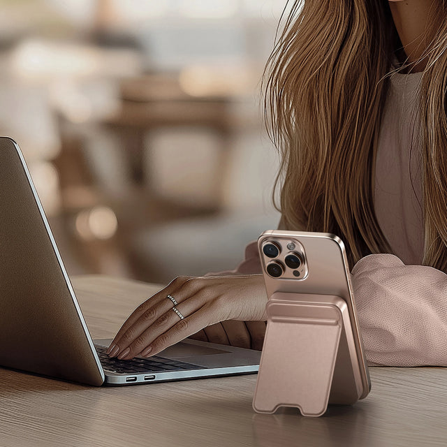 Satechi OntheGo Power Bank 10K holding an iPhone upright beside a laptop, showing its magnetic stand design for hands‑free use while working.