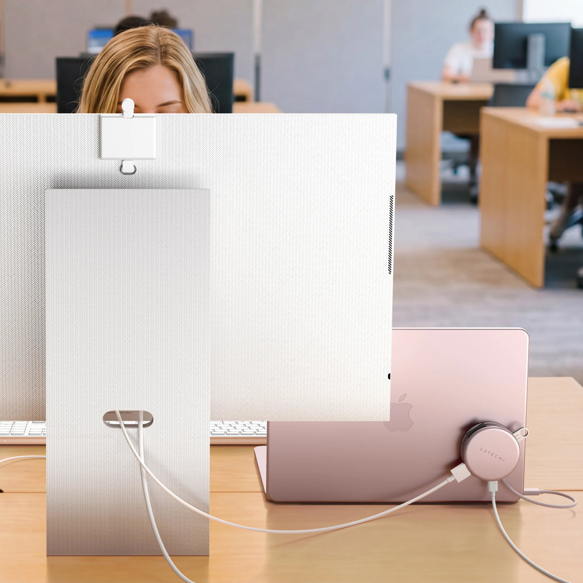 An office desk where a person works behind an external monitor and a Blush MacBook Neo, with a matching Blush Satechi OntheGo™ 5-in-1 Multiport Adapter with power delivery connected to the laptop and cables running to the display. 