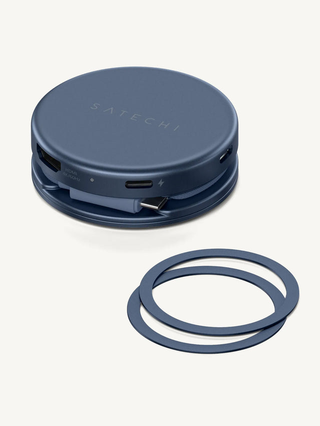Indigo Satechi magnetic USB-C hub shown on a cream background with its wrapped braided cable and USB-C plug stored in the base, beside two matching Indigo magnetic rings. In-image labels read "SATECHI" and "HDMI 4K/60Hz."