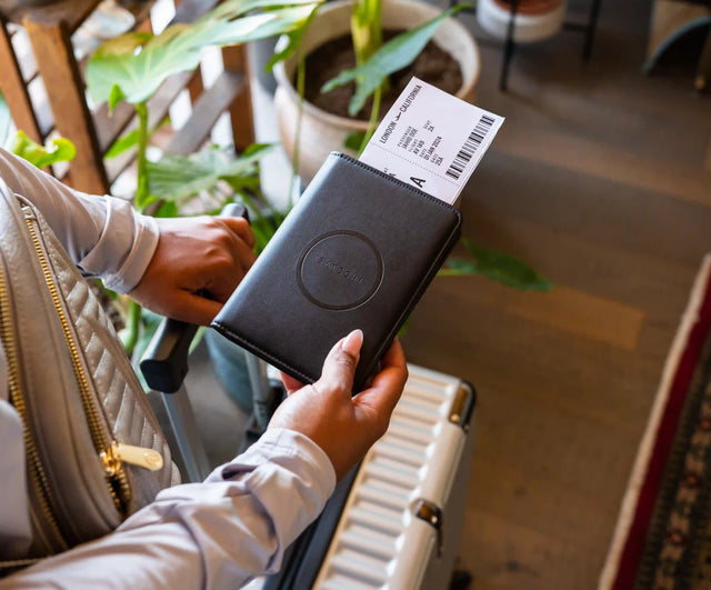 A person holding a closed  Vegan-Leather FindAll™ Passport Cover with plane ticket inside.
