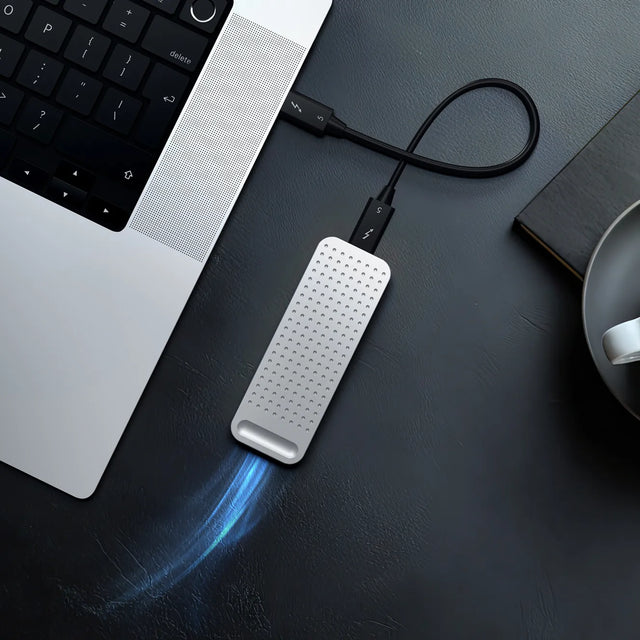 DotDisk™ 80Gbps SSD enclosure connected to a laptop via Thunderbolt cable, slim aluminum portable external NVMe storage on a dark desk, showing the active-cooling feature. 