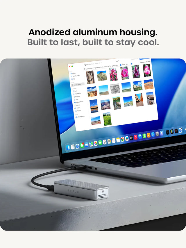 Anodized aluminum housing. Built to last, built to stay cool. Silver Satechi DotDisk portable SSD enclosure connected to a MacBook Pro on a desk, with the Photos app open onscreen displaying imported landscape and floral images from an iPhone.