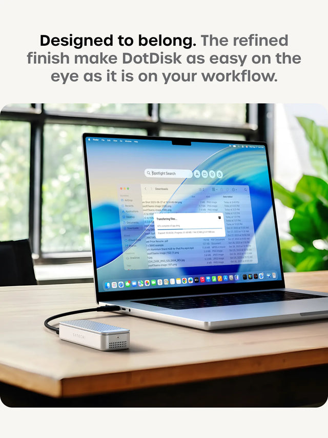 Designed to belong. The refined finish make DotDisk as easy on the eye as it is on your workflow. Close-up detail of the black anodized DotDisk Thunderbolt 5 SSD enclosure on the left. On the right, a MacBook Pro on a wood desk with the silver DotDisk connected, showing a Finder window with a "Transferring files..." dialog at 42% complete.