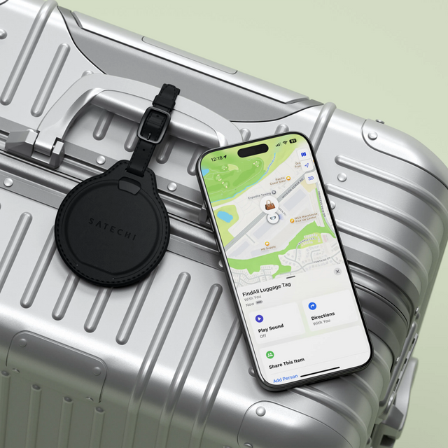Black Satechi Vegan‑Leather FindAll Luggage Tag on a suitcase next to an iPhone showing its location in the Find My app.