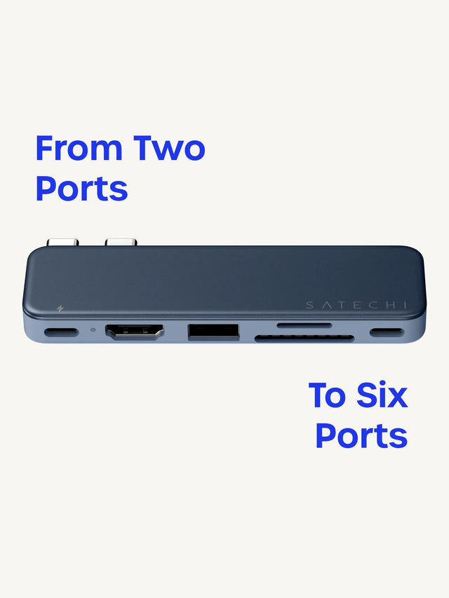 ndigo Satechi USB-C Snap Hub shown front-on against a cream background, with its two USB-C connectors on top and six ports across the front edge — USB-C Power Delivery (charging-bolt icon), HDMI, USB-A, an SD card slot, a microSD slot, and USB-C — with the SATECHI logo on the face. Headline reads "From Two Ports" and "To Six Ports."
