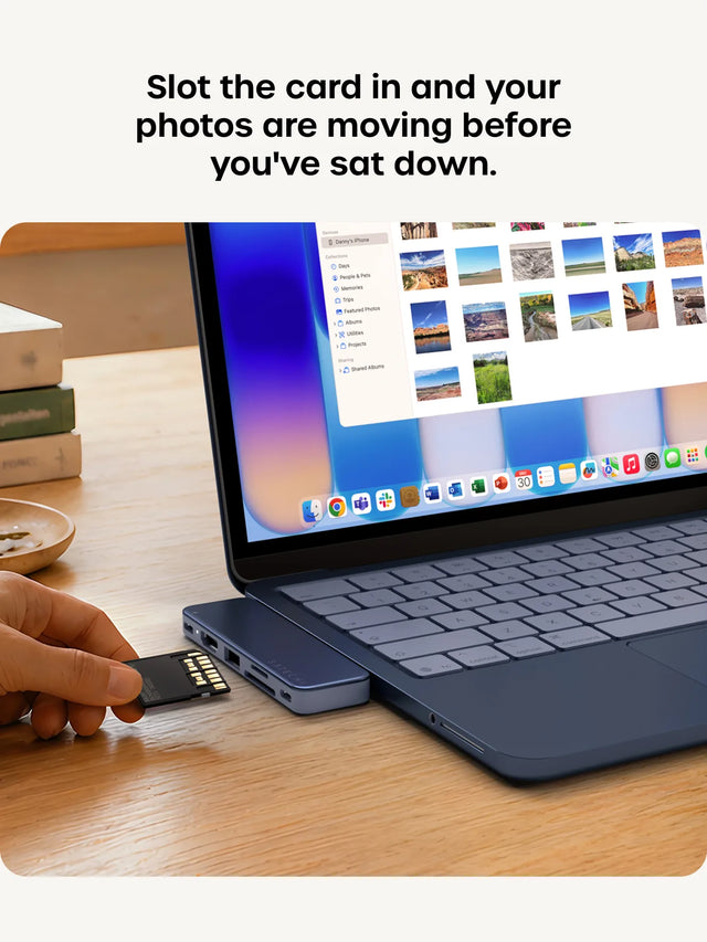 An Indigo MacBook Neo with the macOS Photos app showing "Photos, Library, Recently Saved, Map, Devices, Danny's iPhone" and a grid of photo thumbnails, as a hand inserts an SD card into the attached Indigo USB-C Snap Hub. Right: close-up of a Silver Satechi USB-C Snap Hub with the SATECHI logo, SD slot, USB-A, and USB-C ports. Headline reads "Slot the card in and your photos are moving before you've sat down."