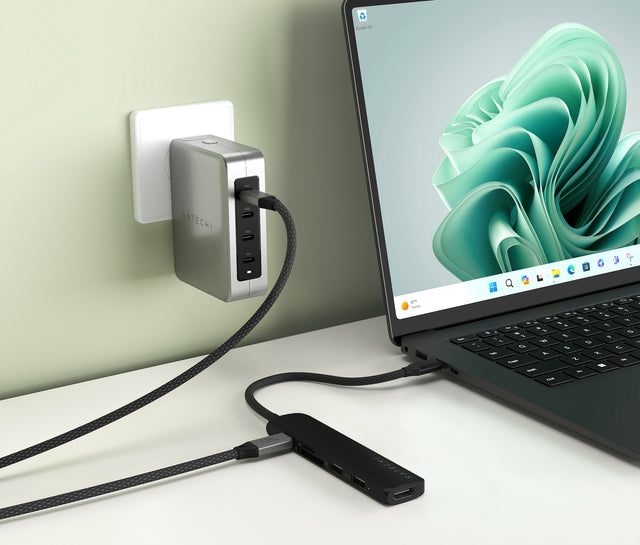 Satechi 6‑in‑1 USB‑C Slim Multiport Adapter connected to a laptop and powered through a wall charger, demonstrating passthrough USB‑C power delivery with multiple connected devices.