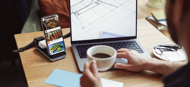 Satechi Duo Wireless Charger Power Stand on a desk charging an iPhone, Apple Watch, and AirPods beside a laptop and a cup of coffee.