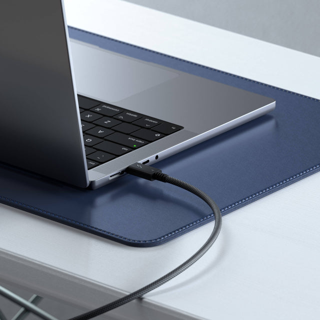 A Satechi Thunderbolt 4 Pro Cable - 1M charging (240W Charging Power) a MacBook on a blue desk mat on a white surface.