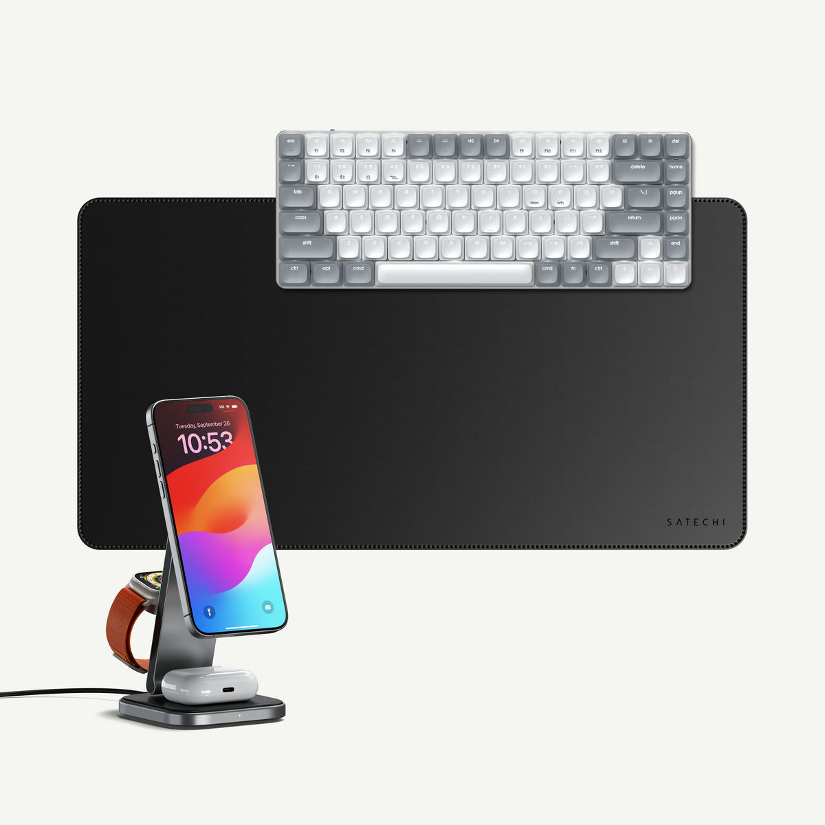 The Power Desk back-to-school bundle: a white-and-gray SM1 slim mechanical keyboard for Mac on a black vegan-leather desk mat, with a 3-in-1 foldable Qi2 wireless charging stand charging an iPhone reading "10:53," an Apple Watch, and AirPods, shown on a light gray background.