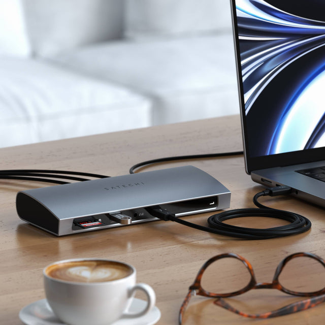 Laptop with Thunderbolt 4 Dock
connected via a thunderbolt cable on a desk next to a cup of coffee and glasses.