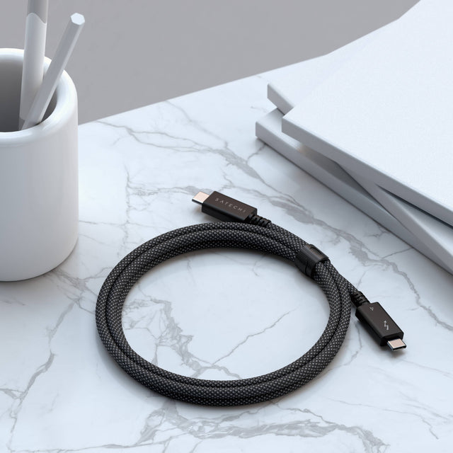 Coiled Satechi Thunderbolt 4 Pro Cable - 1M on a marble surface with a pen holder and books in the background, showing off its durable braided design resists tangles and everyday wear.