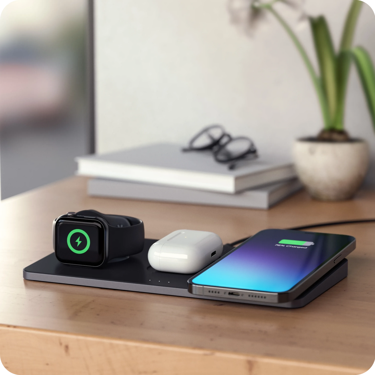 Trio Wireless Charger With Magnetic Pad charging Apple Watch, iPhone, and AirPods on a wooden surface.