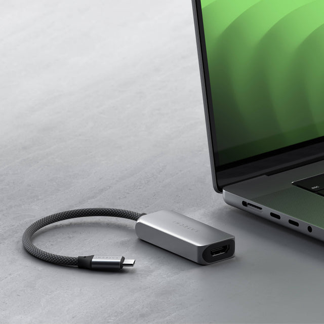 Close‑up of the Satechi USB‑C to HDMI 2.1 8K Adapter placed beside a laptop, showing its braided cable and compact aluminum design.