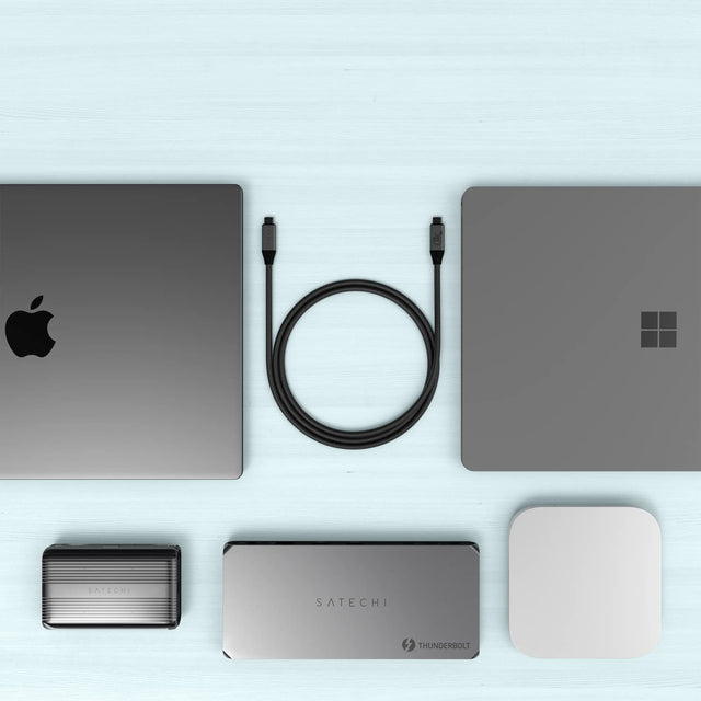 Satechi USB4 V2 Pro Cable coiled on a light blue surface, surrounded by MacBook, laptop, hubs, and SSD enclosures, highlighting universal USB‑C compatibility.