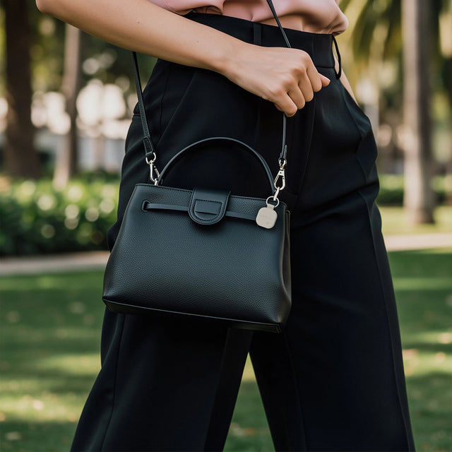 Black handbag with a Sand Satechi Vegan‑Leather FindAll Keychain attached to the strap, shown outdoors on a walkway.